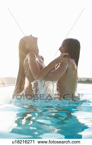 Stock Image - Romantic couple having fun in outdoor swimming pool, man lifting woman. Fotosearch