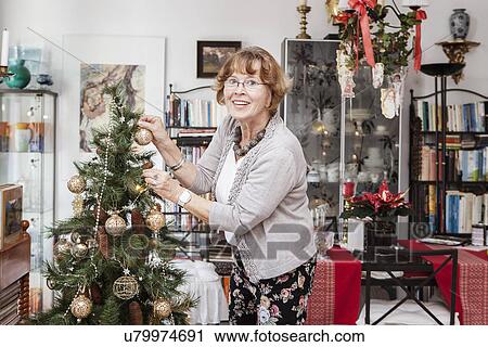 Stock Image - Senior adult woman decorating Christmas tree. Fotosearch