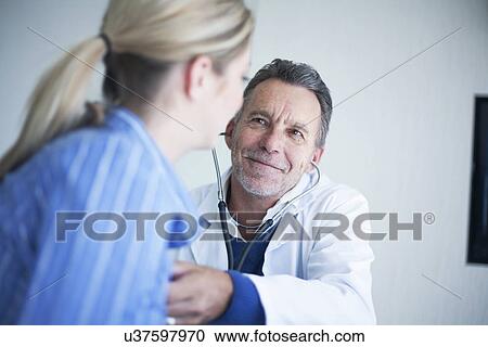 Stock Image - Senior male doctor holding stethoscope to patients chest. Fotosearch
