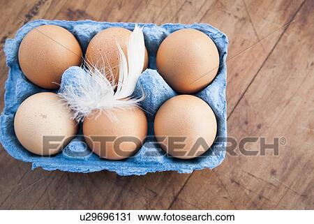 Stock Image - Still life of six brown eggs in blue egg box. Fotosearch