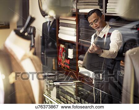 Stock Photo - Tailor looking at fabric in traditional tailors shop. Fotosearch