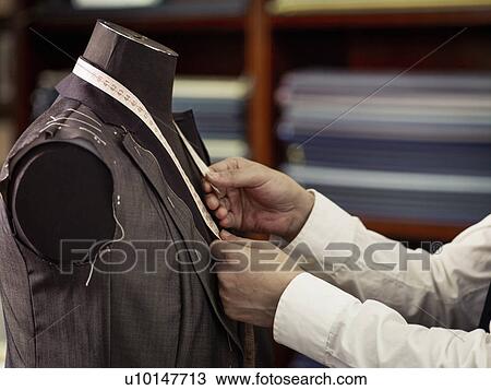 Stock Image - Tailor measuring garment in traditional tailors shop. Fotosearch