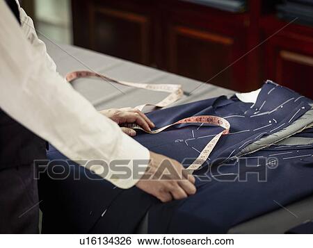 Stock Photograph - Tailor measuring garment on table in traditional tailors shop. Fotosearch