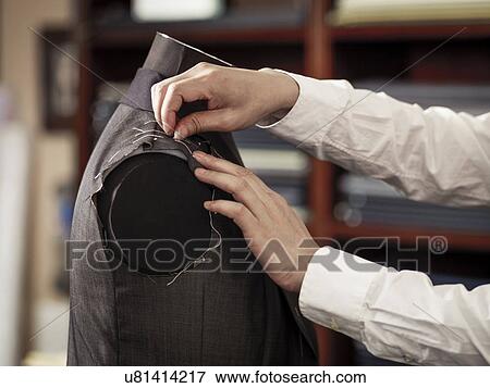 Stock Photo - Tailor pinning garment in traditional tailors shop. Fotosearch