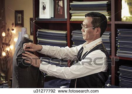 Stock Image - Tailor pinning garment on tailors dummy in shop. Fotosearch