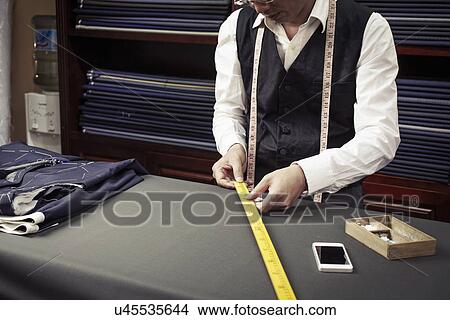 Picture - Tailor taking measurements from ruler in tailors shop. Fotosearch
