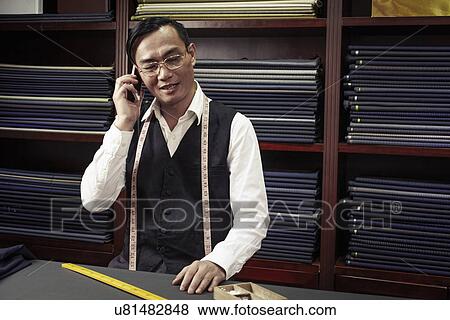 Stock Photo - Tailor talking on cellphone in tailors shop. Fotosearch