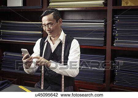 Tailor texting on cellphone in tailors shop View Large Photo Image Stock Image - Tailor texting on cellphone in tailors shop. Fotosearch