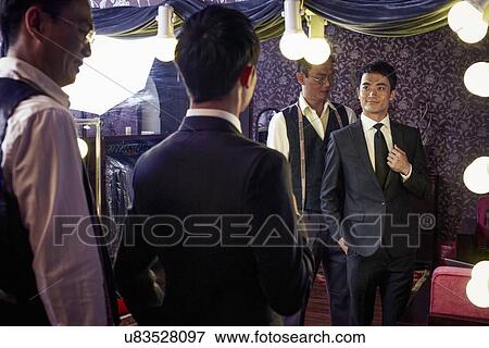 Stock Photo - Tailor with young male client trying on new suit in shop. Fotosearch