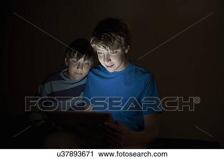 Teenage boy and brother looking at digital tablet at night View Large Photo Image Stock Image - Teenage boy and brother looking at digital tablet at night. Fotosearch