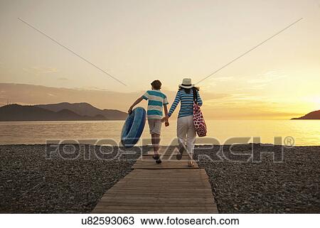 Stock Image - Teenage boy and mother running toward sea, Fethiye, Turkey. Fotosearch