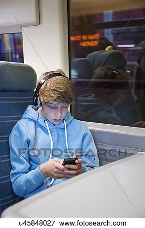 Stock Photo - Teenage boy in headphones and using smartphone on train. Fotosearch