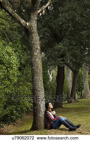 Stock Image - Teenage girl sitting against tree in forest. Fotosearch