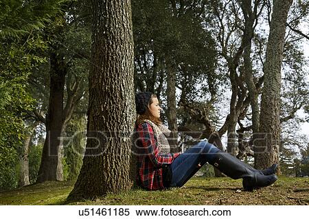 Stock Photography - Teenage girl sitting against tree in forest. Fotosearch
