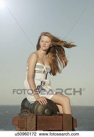 Stock Image - Teenage girl sitting on cannon, Southwold, Suffolk, UK. Fotosearch