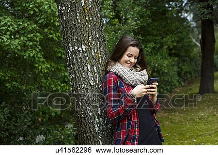 Stock Photograph - Teenage girl using cellular phone in forest. Fotosearch