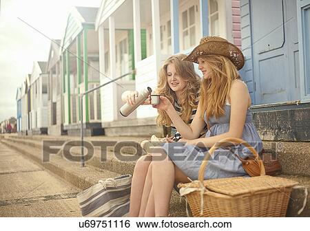 Teenage girls sitting on steps in front of beach hut, drinking flask of tea View Large Photo Image Stock Photograph - Teenage girls sitting on steps in front of beach hut, drinking flask of tea. Fotosearch