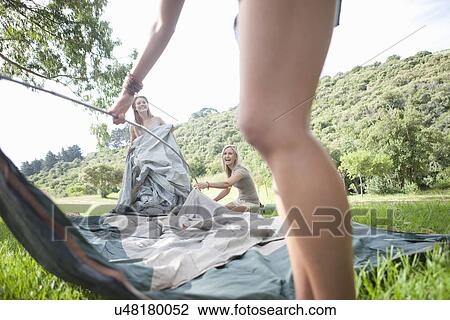 Stock Image - Three friends constructing tent whilst camping. Fotosearch