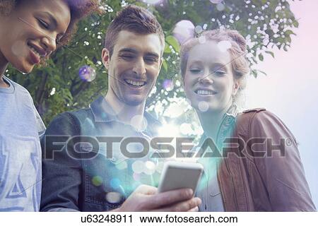 Three friends looking at smartphone with lights coming out of it View Large Photo Image Stock Image - Three friends looking at smartphone with lights coming out of it. Fotosearch