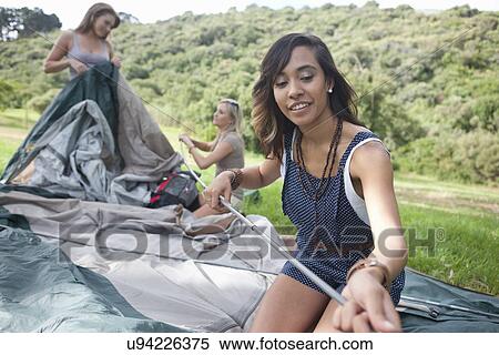 Stock Photography - Three young female friends constructing tent. Fotosearch