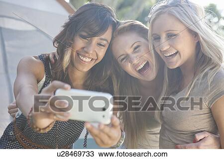 Stock Image - Three young female friends taking a selfie with smartphone. Fotosearch
