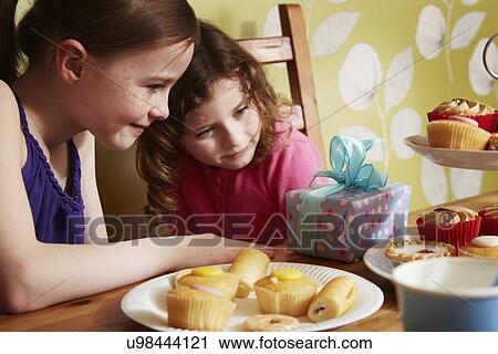 Two girls looking at birthday present with plate of cakes View Large Photo Image Stock Image - Two girls looking at birthday present with plate of cakes. Fotosearch