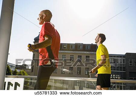 Stock Image - Two male athletes training with skipping ropes on city roof. Fotosearch