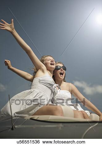 Stock Photograph - Two sisters sitting on back of sports convertible. Fotosearch