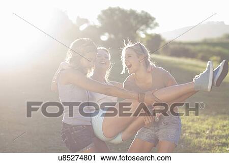Two young females fooling around trying to carry friend View Large Photo Image Stock Image - Two young females fooling around trying to carry friend. Fotosearch
