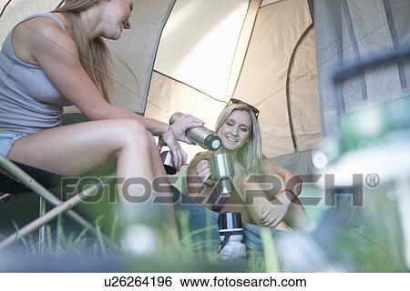 Two young females sharing drinks flask whilst camping View Large Photo Image Stock Photograph - Two young females sharing drinks flask whilst camping. Fotosearch