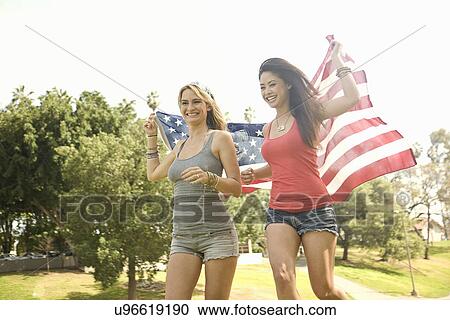 Two young woman running together with american flag in park View Large Photo Image Stock Image - Two young woman running together with american flag in park. Fotosearch