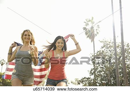 Stock Photo - Two young woman running with american flag in park. Fotosearch