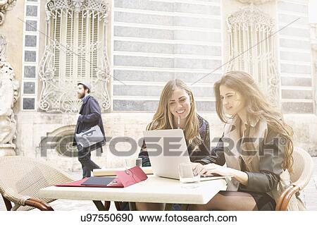 Stock Image - Two young women looking at laptop outside Museum of Ceramics, Valencia, Spain. Fotosearch