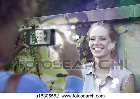 Stock Image - Two young women photographing using smartphone with lights coming out. Fotosearch