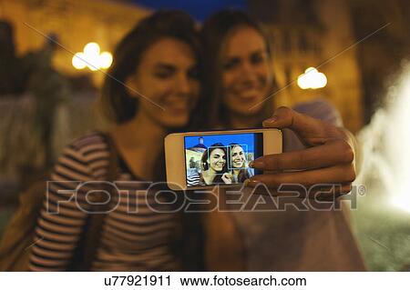 Stock Image - Two young women posing for self portrait, Plaza de la Virgen, Valencia, Spain. Fotosearch