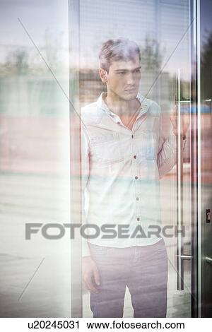 Stock Image - Unhappy young man behind reflective window. Fotosearch