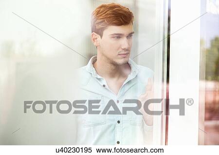 Stock Photography - Unhappy young man looking out of window. Fotosearch