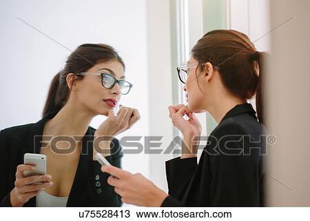 Stock Image - Woman holding phone checking lipstick. Fotosearch