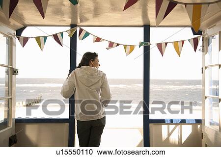 Stock Image - Woman looking out from beach hut, Southwold, Suffolk, UK. Fotosearch