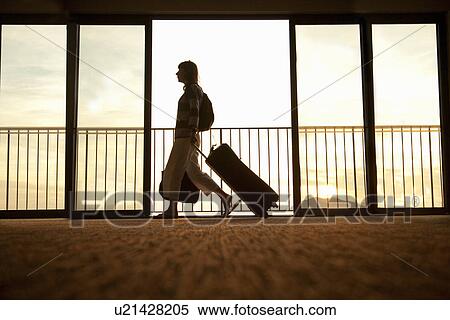 Stock Photography - Woman walking through airport with wheeled suitcase. Fotosearch