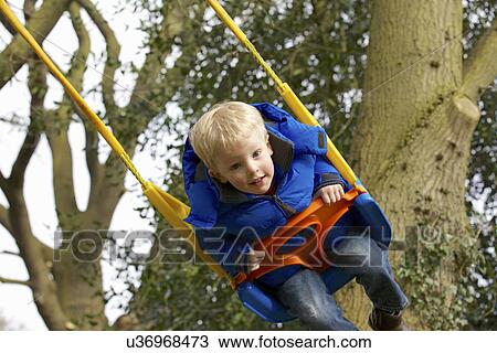 Stock Image - Young boy playing on garden swing. Fotosearch