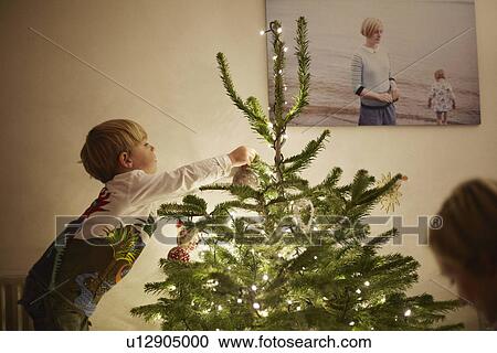Stock Image - Young boy putting lights onto christmas tree. Fotosearch
