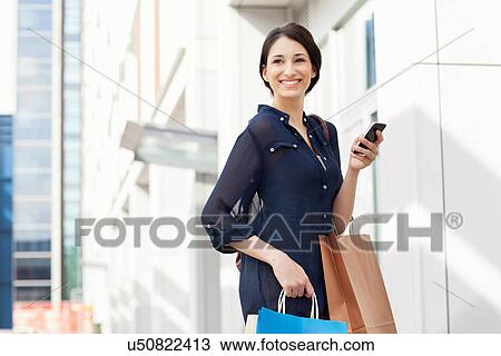 Stock Image - Young businesswoman carrying smartphone and shopping bags. Fotosearch
