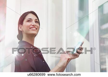 Stock Photo - Young businesswoman holding smartphone with lights coming out of it. Fotosearch