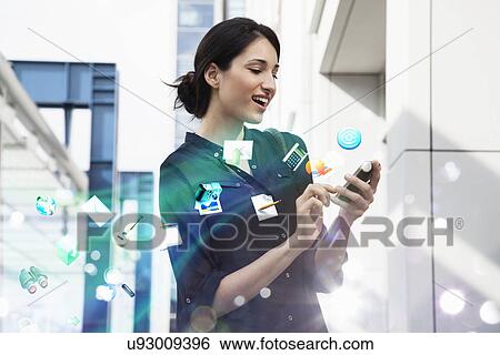 Stock Photograph - Young businesswoman holding smartphone with apps and icons coming out of it. Fotosearch