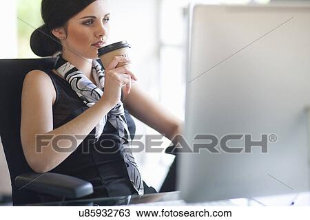 Stock Image - Young businesswoman taking a coffee break at desk. Fotosearch