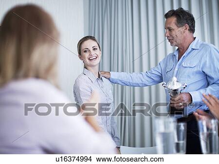 Picture - Young businesswomen receiving trophy at meeting. Fotosearch