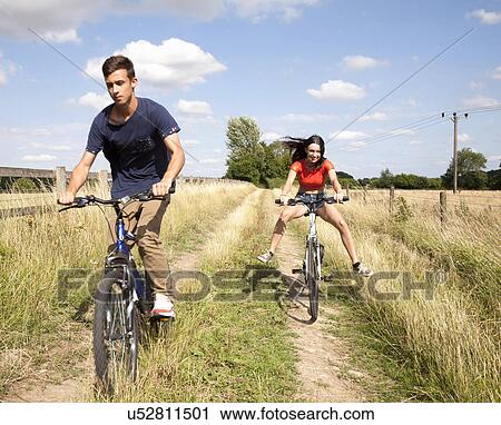 Young couple cycling through field on dirt track View Large Photo Image Stock Image - Young couple cycling through field on dirt track. Fotosearch