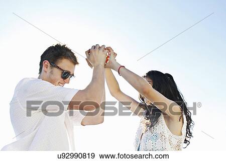 Stock Photo - Young couple holding hands with arms raised. Fotosearch