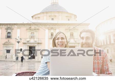 Young couple looking at laptop in sidewalk cafe, Plaza de la Virgen, Valencia, Spain View Large Photo Image Stock Photography - Young couple looking at laptop in sidewalk cafe, Plaza de la Virgen, Valencia, Spain. Fotosearch